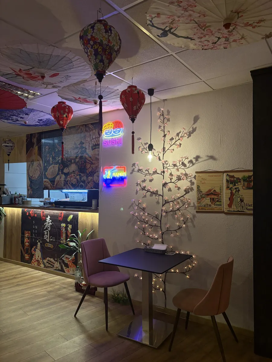 Gemütlicher Zweiertisch mit Kirschblütenbaum und Neonschildern Sushi und Ramen