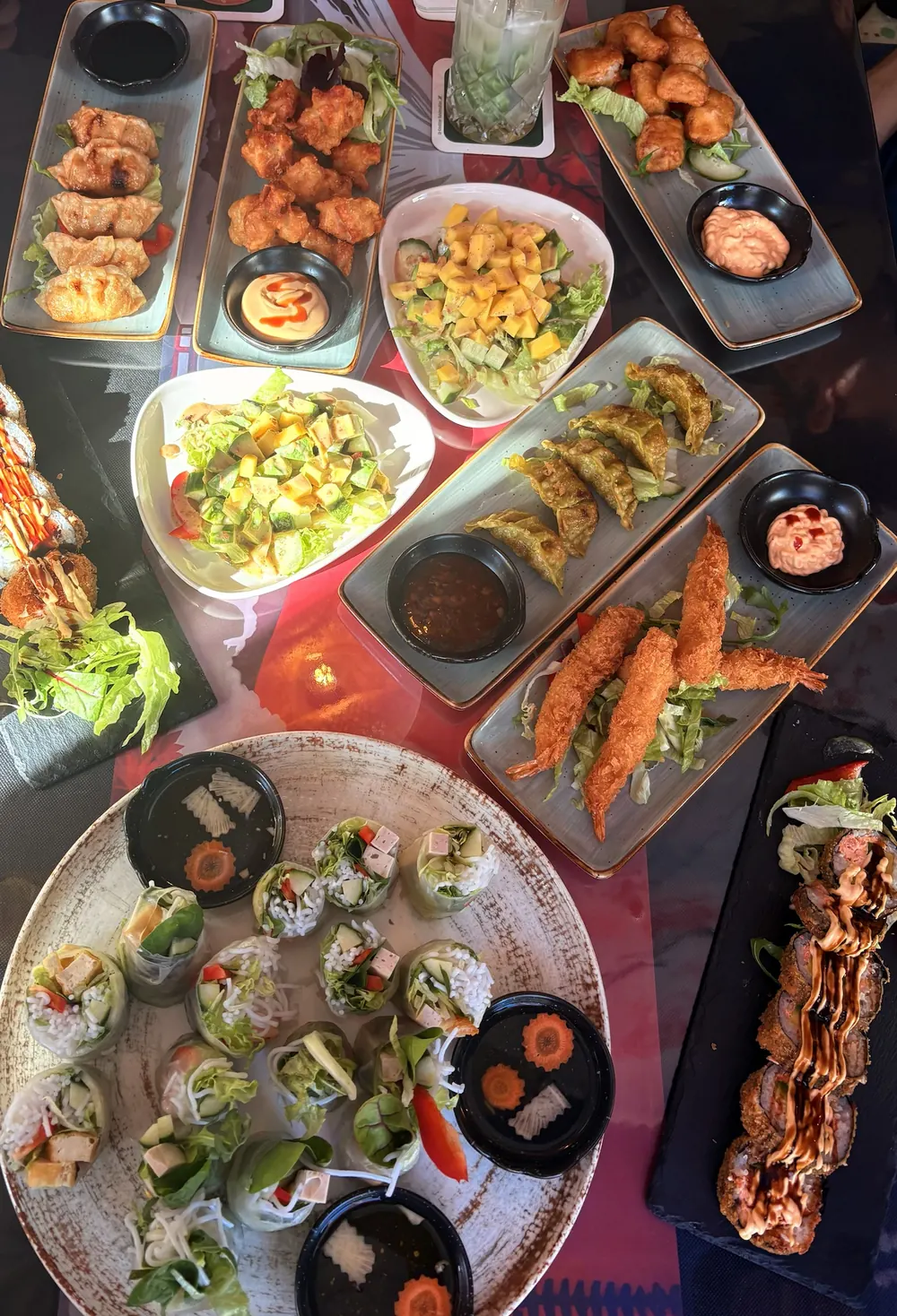 Gedeckter Tisch mit Gyoza, Chicken Karaage, Mangosalat, Tempura-Garnelen, Sommerrollen und Crunchy Rolls
